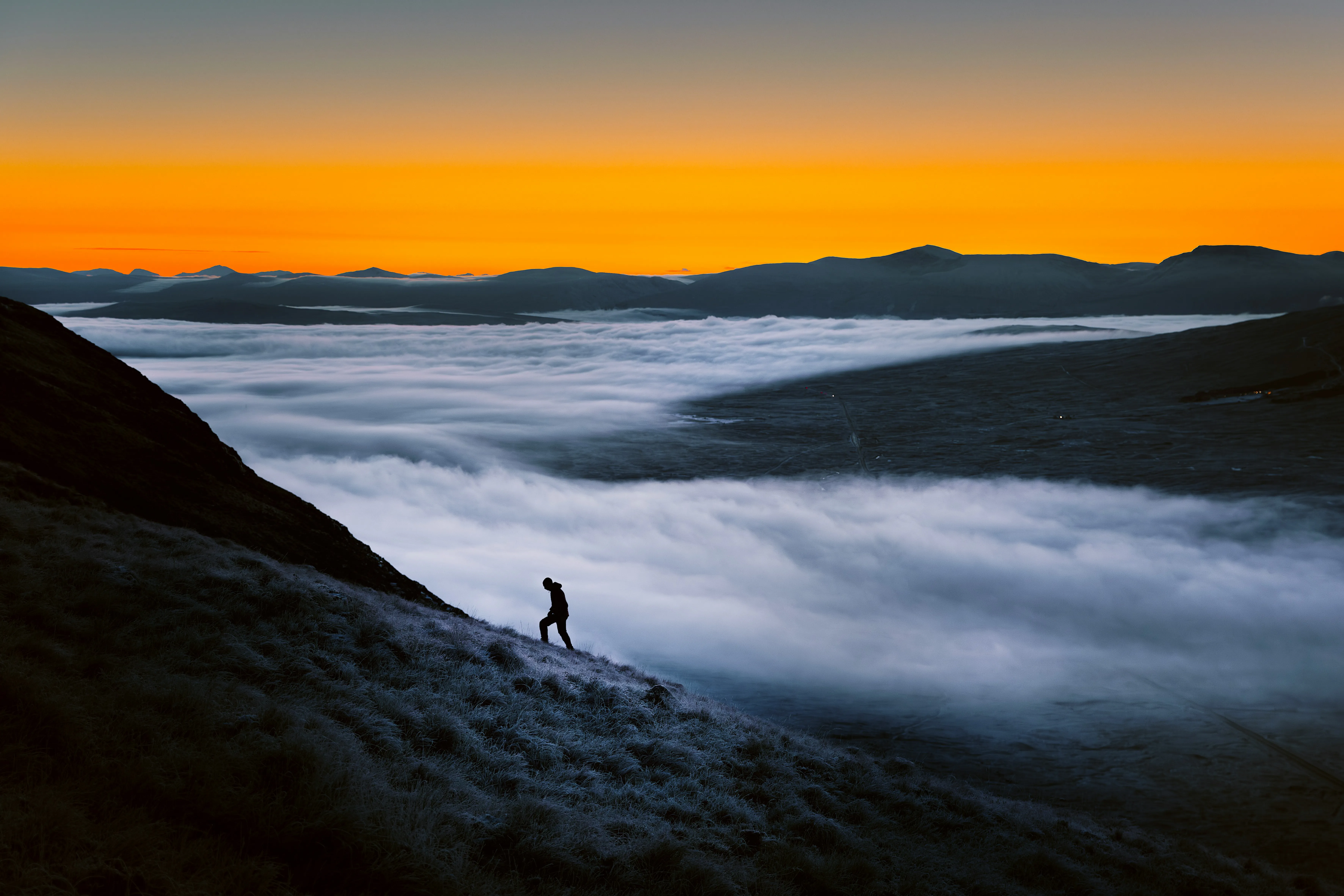 Man climbing through fog toward sunrise on mountain ridge