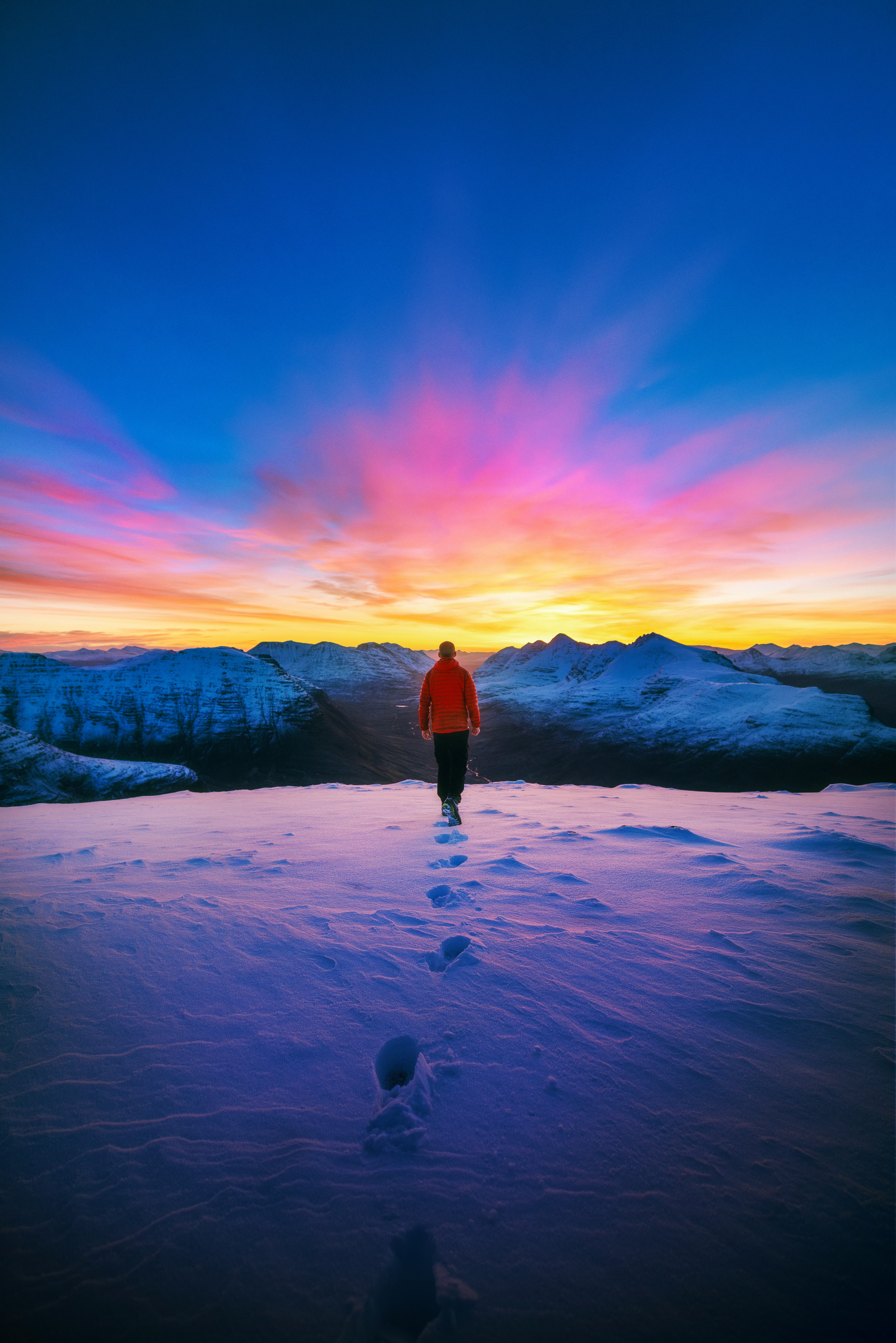 Man walking toward sunrise through snow-covered landscape