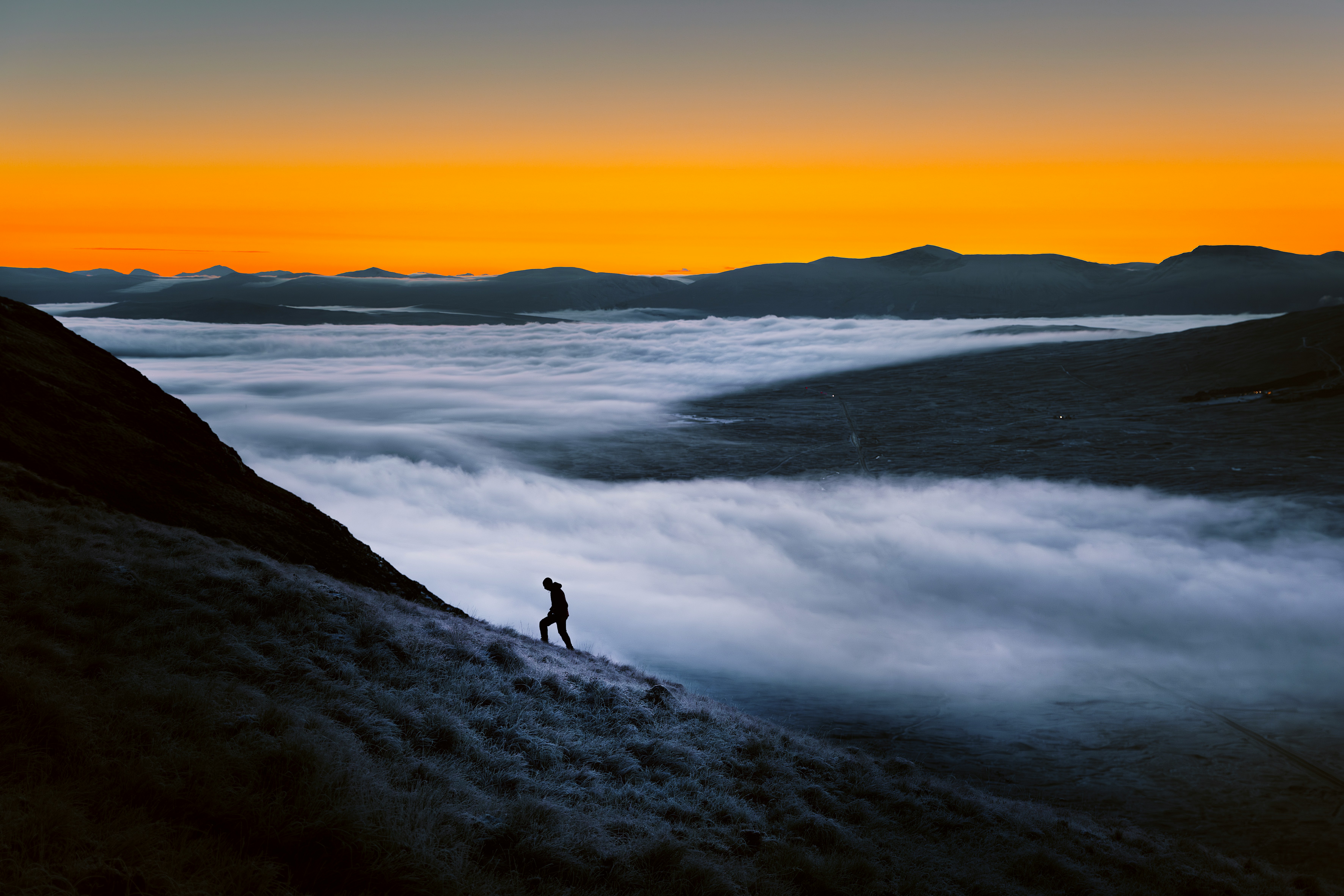 Man climbing through fog toward sunrise on mountain ridge